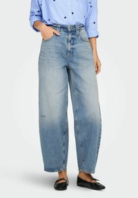 Vaqueros de tiro alto de color azul claro con un ajuste relajado de pierna ancha y un ligero desgastado. Combinados con una camisa de botones a rayas azul.
