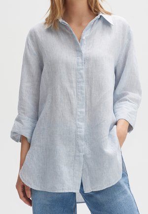 Camisa de botones rayada en azul claro con cuello, mangas enrolladas y un corte relajado, hecha de una tela texturizada. Combinada con jeans.