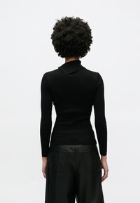 Schwarzer, gerippter Strickpullover mit langen Ärmeln und flachem Kragen. Kombiniert mit hoch taillierter, schwarzer Lederhose mit Gesäßtaschen.