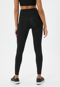Svarta högmidjade leggings med en slät yta och figurnära design, med en sömlös bakdel och minimal sömnadsdetalj.