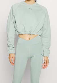 Felpa corta verde chiaro con orlo e polsini elasticizzati, con un piccolo logo sul petto, abbinata a leggings a vita alta coordinati.