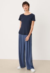 Marineblauw t-shirt met korte mouwen en een ronde hals, gecombineerd met lichtblauwe wijde broek en witte sneakers, op een neutrale achtergrond.