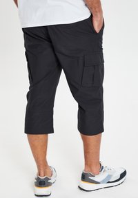 Zwarte cargoshorts met een knielang ontwerp, voorzien van zijzakken en een relaxte pasvorm. G gedragen met casual sneakers.