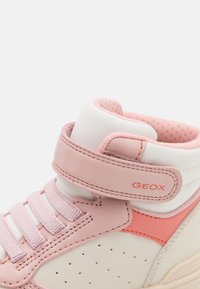 Close-up van een witte en roze hoge sneaker met een gevoerd kruis, een klittenbandsluiting met het label "GEOX," en elastische veters.