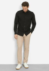 Zwarte lange mouwen shirt met een knoopsluiting aan de voorkant, gecombineerd met beige broek en witte sneakers. Gladde stof en op maat gemaakte pasvorm.