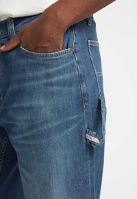 Lichte blauwe denim jeans met een vervaagde textuur, voorzien van een voorzak en een zichtbaar merklabel aan de zijkant.