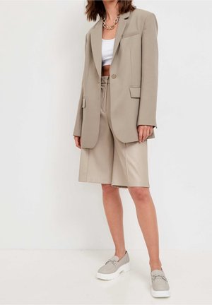 Blazer beige ajusté avec un bouton unique, assorti avec un short beige. Porté avec un haut blanc et des chaussures à plateforme gris clair.