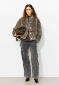 Veste bomber en fausse fourrure gris olive avec décolleté rond, boutons-pression, associée à un jean gris ample et un sac vert foncé. Bottines noires.