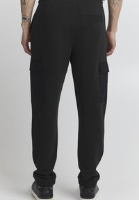 Black cargo pants made of cotton, featuring two side pockets, elastic waistband, and ribbed cuffs. Simple design with side cargo pockets.