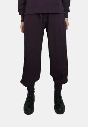 Pantaloni della tuta viola con vestibilità rilassata, dotati di vita elastica e polsini, abbinati a stivali neri con lacci. Tessuto dalla texture morbida.
