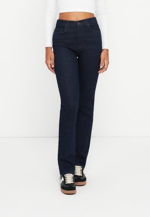 Dark blue high-waisted jeans with a fitted silhouette, two front pockets, and a zip fly. Paired with black sneakers featuring white laces.