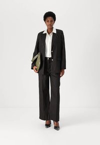 Black and gold pinstriped suit jacket and trousers paired with a white shirt. Accessories include a green bag and black pointed shoes.