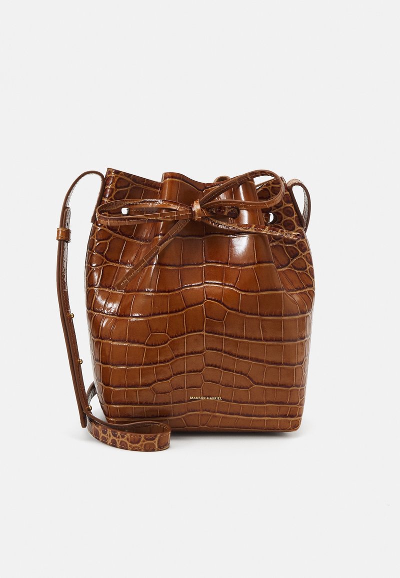 Bolso bucket de cuero marrón con un patrón de cocodrilo, cierre de cordón y una correa larga ajustable. Acentos en hardware dorado visibles.