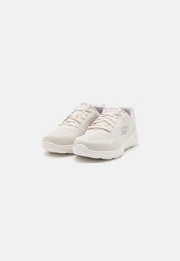 White mesh athletic shoes with a textured surface, laces, and a light purple logo detail. Rounded rubber sole for cushioning.