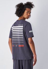 Camiseta de algodón azul marino con rayas blancas horizontales, un logotipo en la parte trasera y detalles en rojo. Con mangas cortas y un diseño de corte relajado.