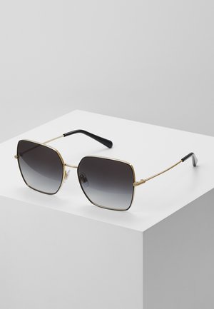 Lunettes de soleil avec une monture en métal doré, des verres carrés qui passent d'un gris foncé à un gris clair, et des branches en plastique noir.