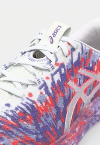 Shoe with a textured white upper featuring a red and purple abstract pattern, gray accents, and a logo on the tongue and side.