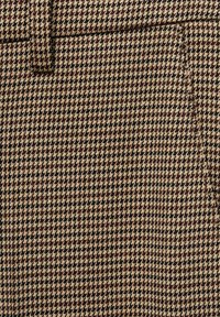 Hnědá látka s motivem houndstooth se strukturovaným tkaním, s naproti sobě se střídajícími světlými a tmavými vzory, vytvářející klasický károvaný design.