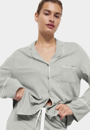 Camisón gris hecho de un tejido suave con un cierre de botones en el frente, ribete blanco y un bolsillo en el lado izquierdo del pecho. Mangas largas con puños.