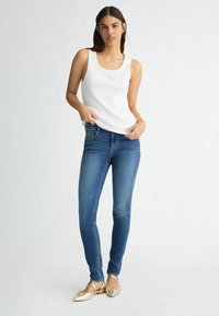 Top in cotone bianco a coste con scollatura a girocollo, abbinato a jeans slim blu scuro e ballerine dorate. Design semplice, senza motivi degni di nota.