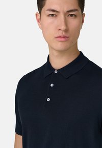 Polo de manga corta en azul marino con tejido texturizado, cuello clásico y tapeta con tres botones blancos.