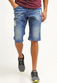 Džínové šortky ve světle modré barvě s opotřebovanými detaily. Mají volný střih a lem přímo nad koleny. V kombinaci se šedými teniskami.