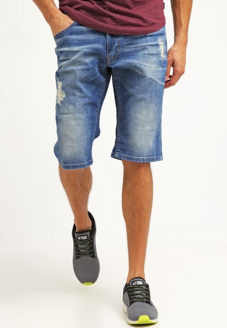 Džínové šortky ve světle modré barvě s opotřebovanými detaily. Mají volný střih a lem přímo nad koleny. V kombinaci se šedými teniskami.