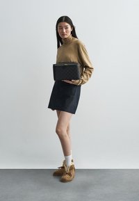 Czarna pikowana torebka z złotym zamkiem, noszona z beżową bluzką z długim rękawem, ciemnoniebieską spódnicą dżinsową i brązowymi kozakami za kostkę z futerkiem. Widoczne białe skarpetki.