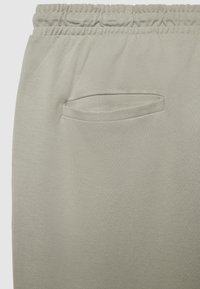 Pantaloni grigio chiaro con tessuto strutturato, vita elastica e una piccola tasca laterale discreta. Il design è casual e pratico.