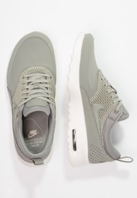 Sneakers Nike con una toma superiore in mesh grigio chiaro, punta grigia solida, suola bianca e dettagli di ammortizzazione d'aria nel tallone.