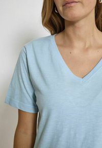 T-shirt azzurro chiaro a maniche corte, con scollo a V, realizzato in un tessuto morbido e testurizzato. Presenta una vestibilità rilassata e dettagli di cucitura minimi.