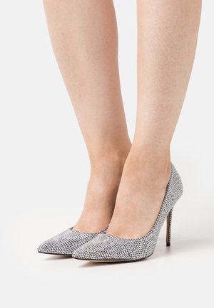 Teräväkärkiset korkeakorkoiset kengät hopeisesta kankaasta, joissa on strassikoristeluja. Varustettu kapealla stilettokannalla ja sileällä pintarakenteella.