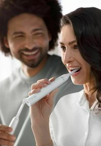 Spazzolino elettrico con manico bianco, design sottile e testa dell'applicatore angolata. L'utente tiene il dispositivo mentre si spazzola i denti.