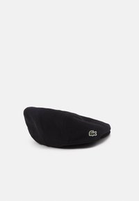 Béret en laine noir avec une texture lisse et un logo crocodile vert Lacoste brodé sur le côté. Forme ronde et plate avec une finition douce.