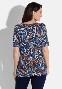 Kurzärmliges, farbenfrohes Oberteil mit einem wirbelnden Muster in Blau, Orange und Weiß auf einem navy Hintergrund; aus weichem Stoff gefertigt.