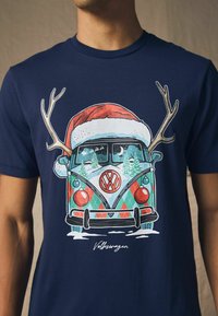 Marineblå t-shirt med et Volkswagen varevogn grafisk design, der har en rød og hvid julestråle, gevir og farverige dekorative detaljer.