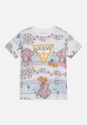 T-shirt blanc à manches courtes avec motifs floraux et citron, illustration d’une ville côtière, ours en peluche dans des voitures, et un grand logo orange Guess.