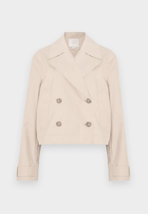 Beige cropped dobbelspent jakke med store slag, to sidelommer og knappedetaljer. Laget av et glatt, lett stoff.