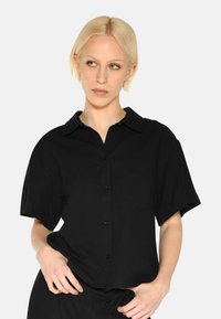 Black short-sleeve shirt with a collared neckline, buttons down the front, and a chest pocket. Smooth fabric with a relaxed fit.