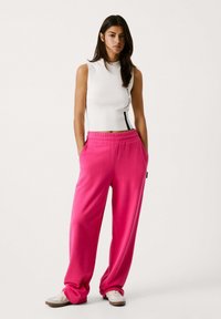 Lyserøde sweatpants med elastisk talje og sidelommer, parret med en tætsiddende hvid ærmeløs top med sorte detaljer.