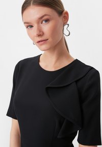 Czarna sukienka z krótkimi rękawami, z warstwowym falbaną wzdłuż dekoltu. Gładki materiał, dopasowany krój, minimalistyczny styl.