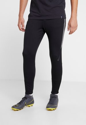 Svarta sportleggings med slim fit, med en reflekterande sidostrip, parat med grå fotbollsskor och en mörk t-shirt.