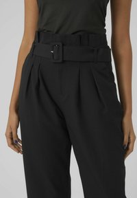 Pantalons larges noirs avec une taille haute, dotés d'une ceinture en tissu, de plis et d'une texture lisse.