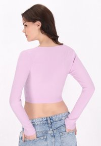 Top scurt cu maneci lungi, de culoare lila, cu guler rotund, având mâneci ajustate și o textură fină. Purtați-l cu șorturi din denim cu talie înaltă.