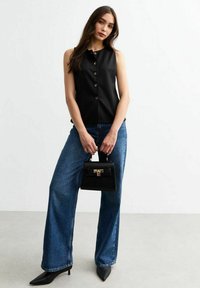 Svart ärmlös topp med knäppning, matchad med vida blå denimjeans och en liten svart handväska. Spetsiga svarta klackar bärs.
