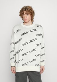 Weißer, gestrickter Pullover mit schwarzem "CARLO COLUCCI" Textmuster, Rundhalsausschnitt und gerippten Bündchen. Lockere Passform mit überschnittenen Schultern.