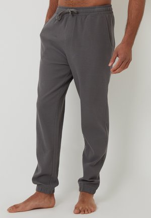 Pantalons de jogging gris en tissu doux, avec une taille élastique à cordon, des chevilles fuselées et des poches latérales. Texture lisse avec des poignets côtelés.