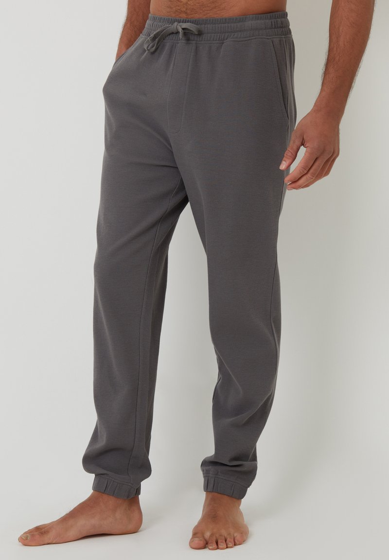 Pantaloni jogger grigi realizzati in morbido tessuto, con vita regolabile tramite cordino, caviglie affusolate e tasche laterali. Tessuto liscio con polsini a costine.