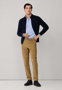 Marineblauer Reißverschluss-Pullover über einem hellblau- und weiß gestreiften Hemd, beigen Chinos und marineblauen Wildlederschuhen. Saubere Linien und klassischer Schnitt.