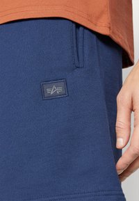 Pantalons de survêtement bleu marine en tissu doux, avec un patch logo brodé, des poches latérales et une surface lisse et texturée.